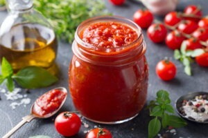 Tomato sauce in a glass jar with fresh herbs, tomatoes and olive oil.