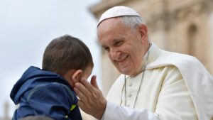 Papa Francisc zâmbește și mângăie un copil