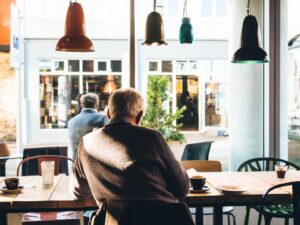 Un bătrân stă pe scaun la o masă într-o cafenea