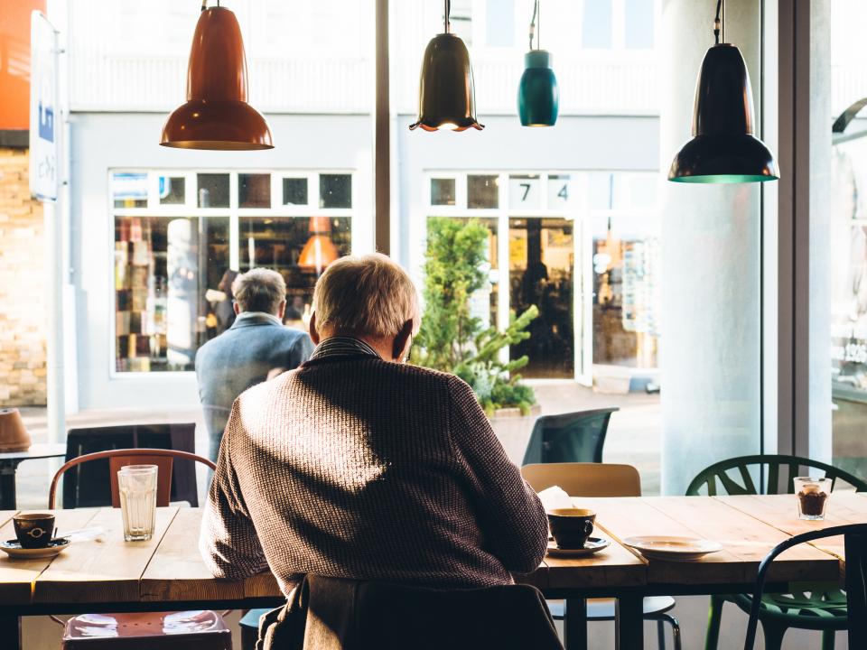 Un bătrân stă pe scaun la o masă într-o cafenea