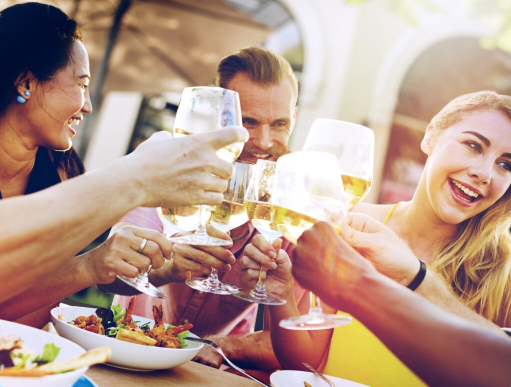Tineri care beau un pahar de vin la masa și zâmbesc