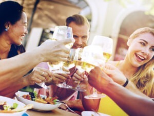 Tineri care beau un pahar de vin la masa și zâmbesc